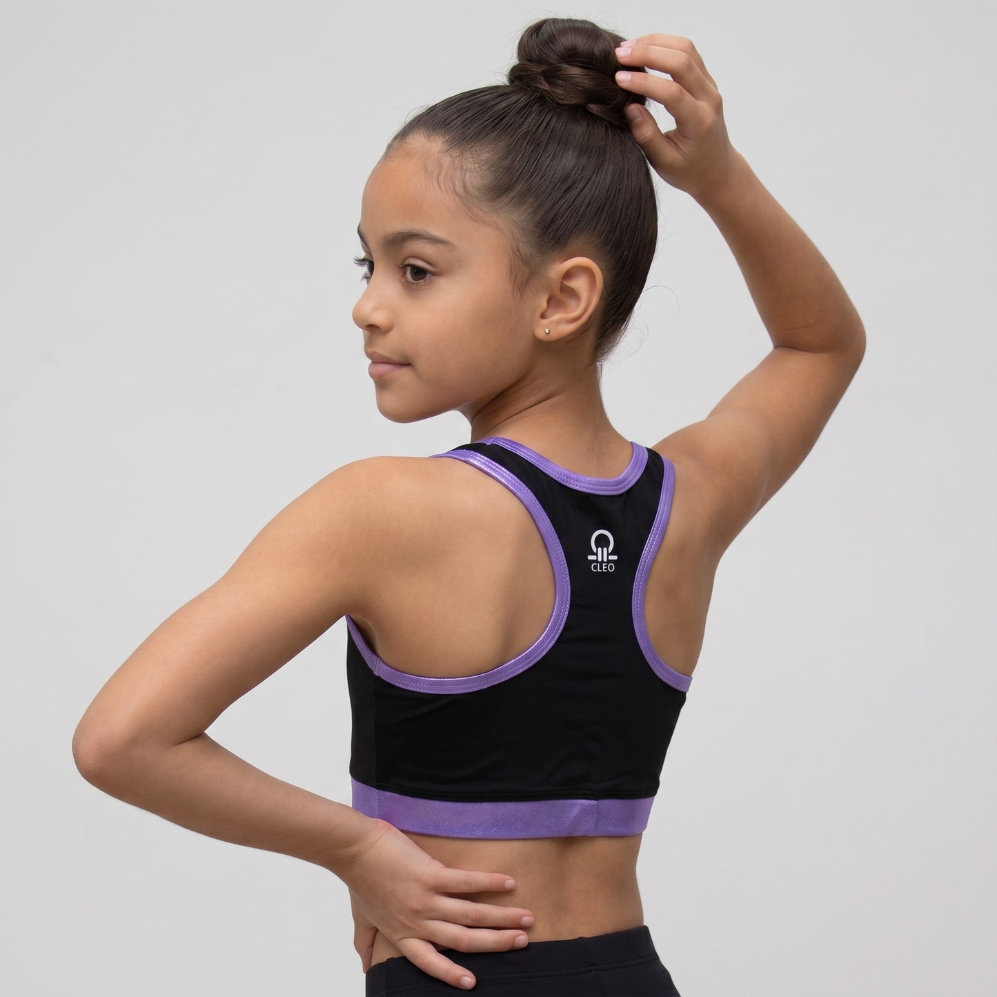 Young girl wearing a black and purple sports bra with a visible brand logo on a light gray background.