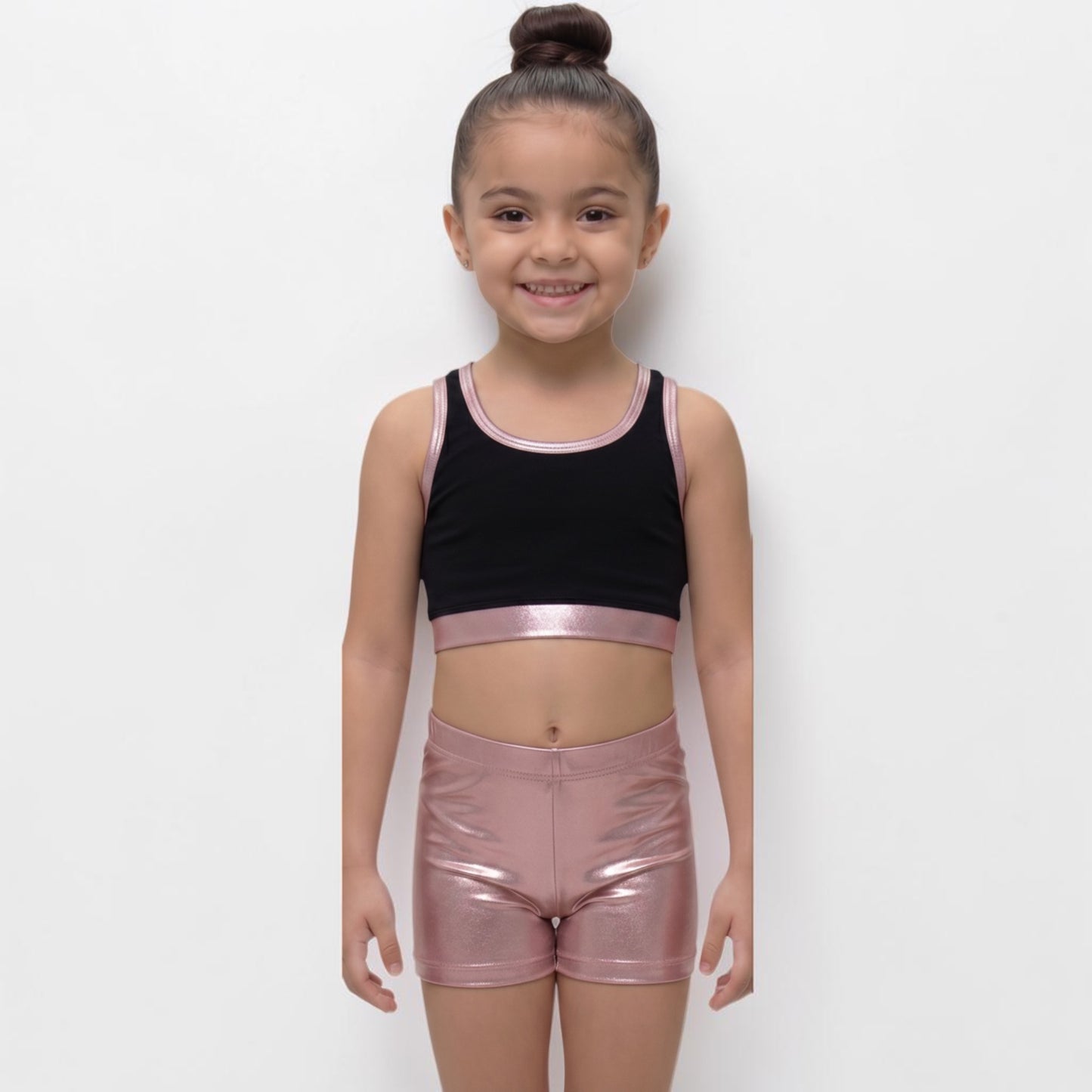 Young girl wearing a black crop top and pink metallic shorts on a white background