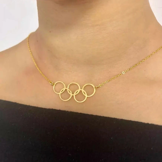 A close-up image of a woman wearing a gold-plated stainless steel necklace with a minimalist Olympic rings design.