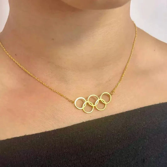 A close-up image of a gold-plated stainless steel necklace with three interlocking rings pendant, inspired by the Olympic rings design, worn by a person.