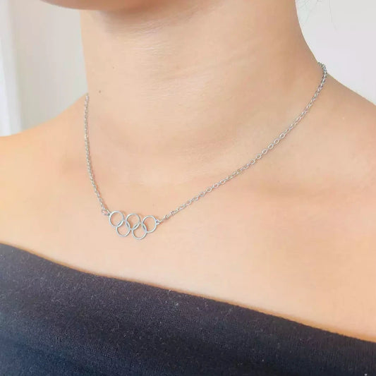 A person wearing a black top and showcasing a silvery stainless steel necklace with a minimalist Olympic rings design.