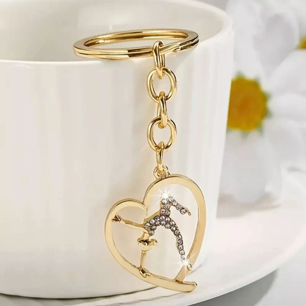 A golden keychain with a shiny stone designed in the shape of a gymnastics icon, placed on a white cup.