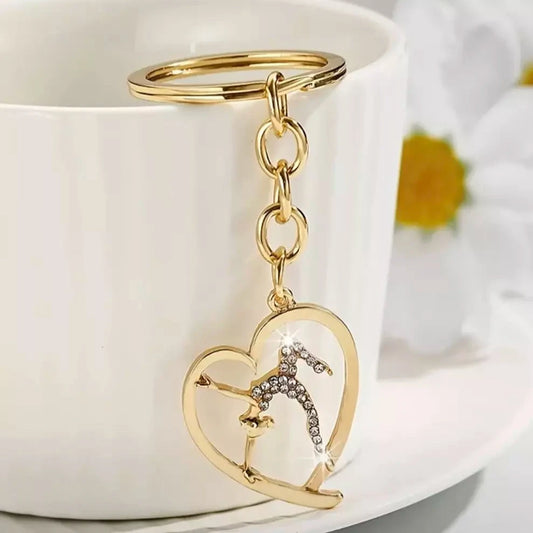 A golden keychain with a shiny stone designed in the shape of a gymnastics icon, placed on a white cup.