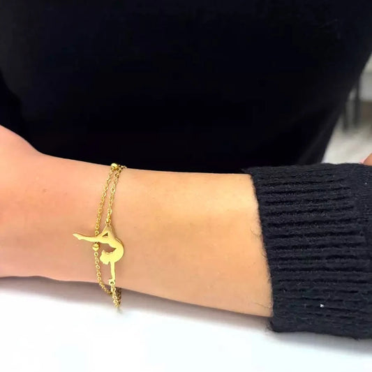 A gold-plated stainless steel bracelet with a gymnastics theme, featuring an adjustable length, being worn on a person's wrist.