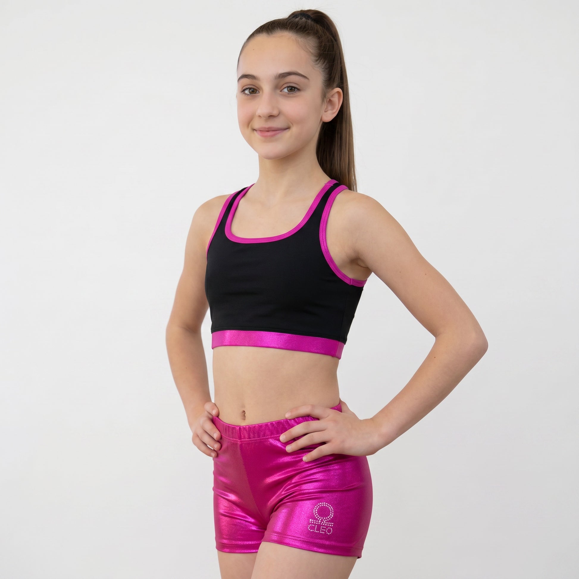 Young girl wearing a black sports bra with pink trim and pink shorts on a white background