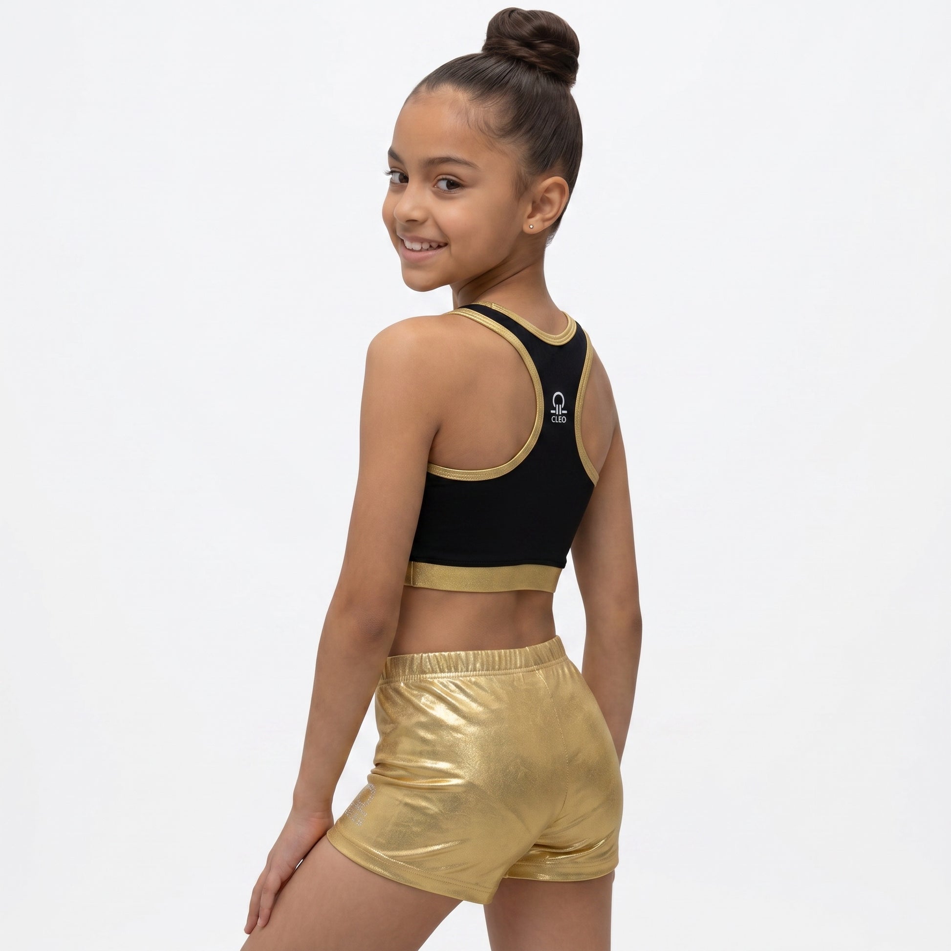 Young girl wearing a black sports bra and gold shorts on a white background