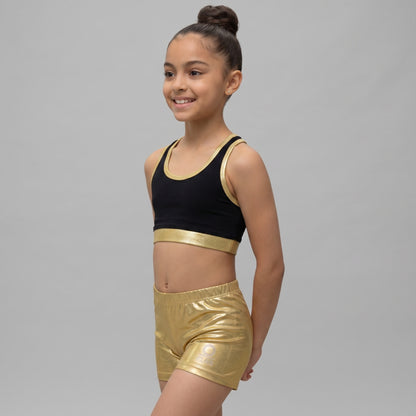 Young girl wearing a black and gold sports bra and shorts on a gray background