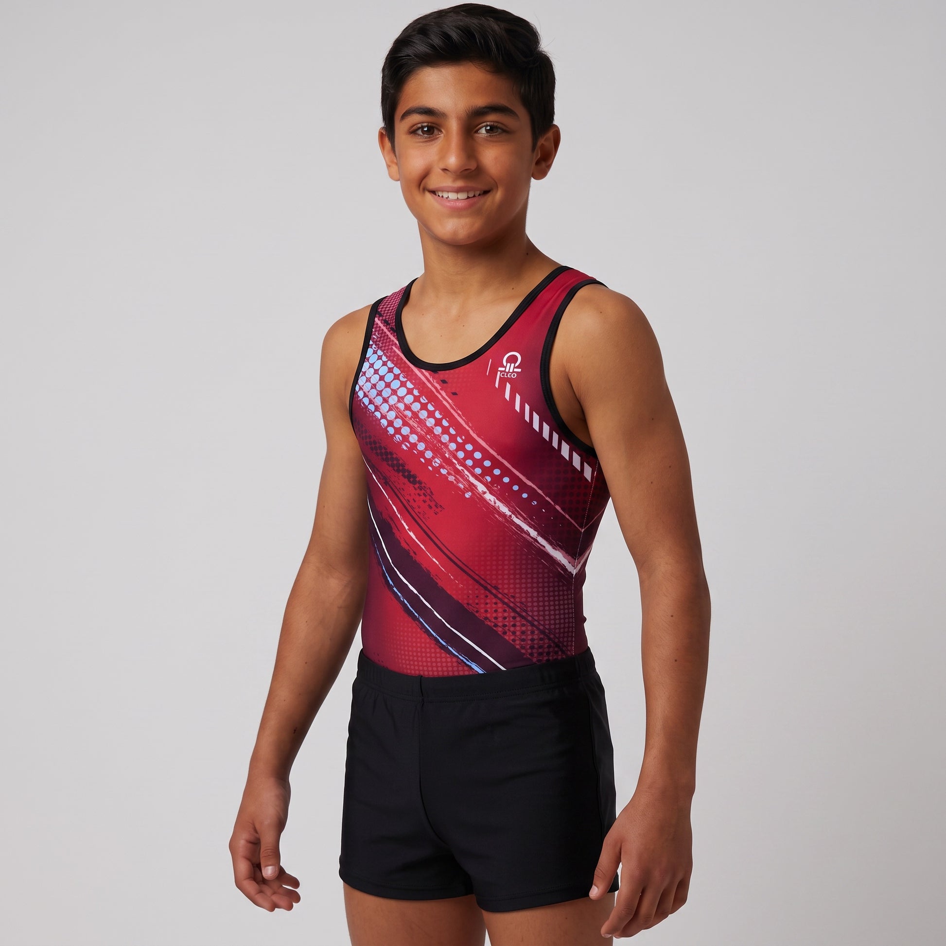A young male gymnast wearing a red and black sleeveless leotard with a geometric pattern and black athletic shorts, standing against a light gray studio background.