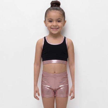 Young girl wearing a black crop top and pink metallic shorts on a white background