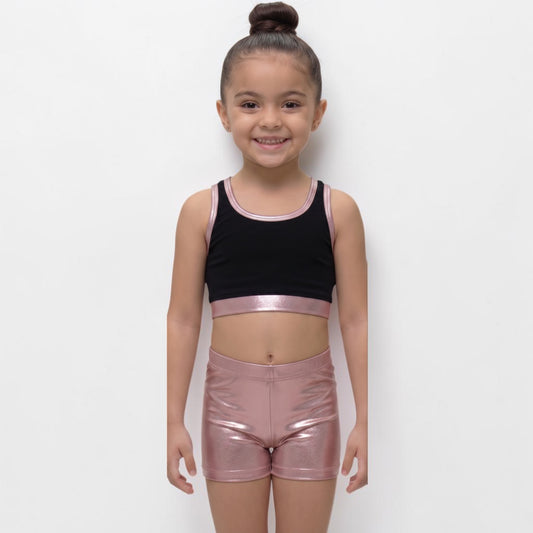 Young girl wearing a black crop top and pink metallic shorts on a white background