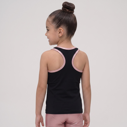 A young girl with her hair in a high bun is shown from the back, wearing a black athletic tank top with light pink trim around the shoulder straps and neckline, paired with matching pink athletic shorts, against a light gray studio background.