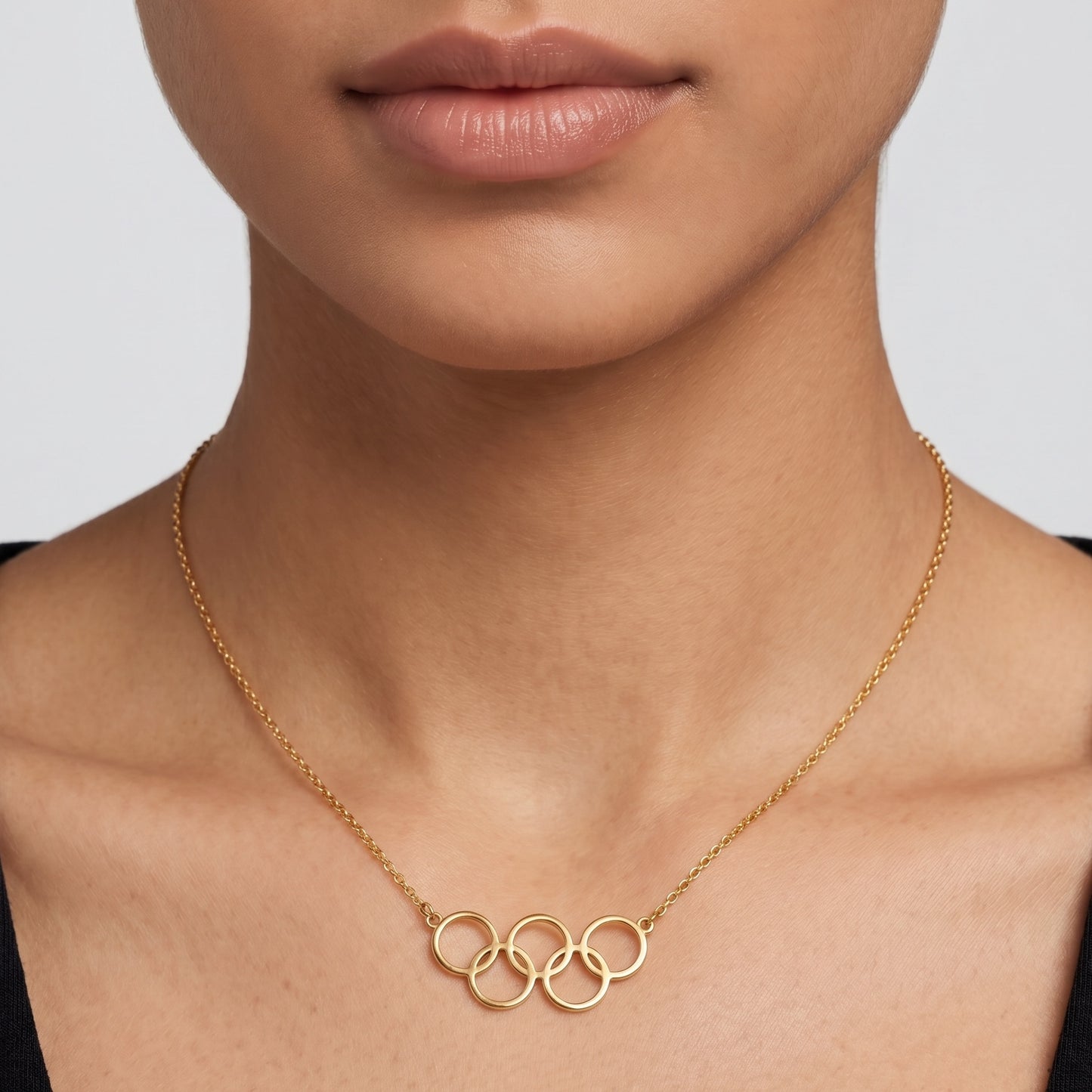 Gold necklace with interlocking rings worn by a person against a neutral background
