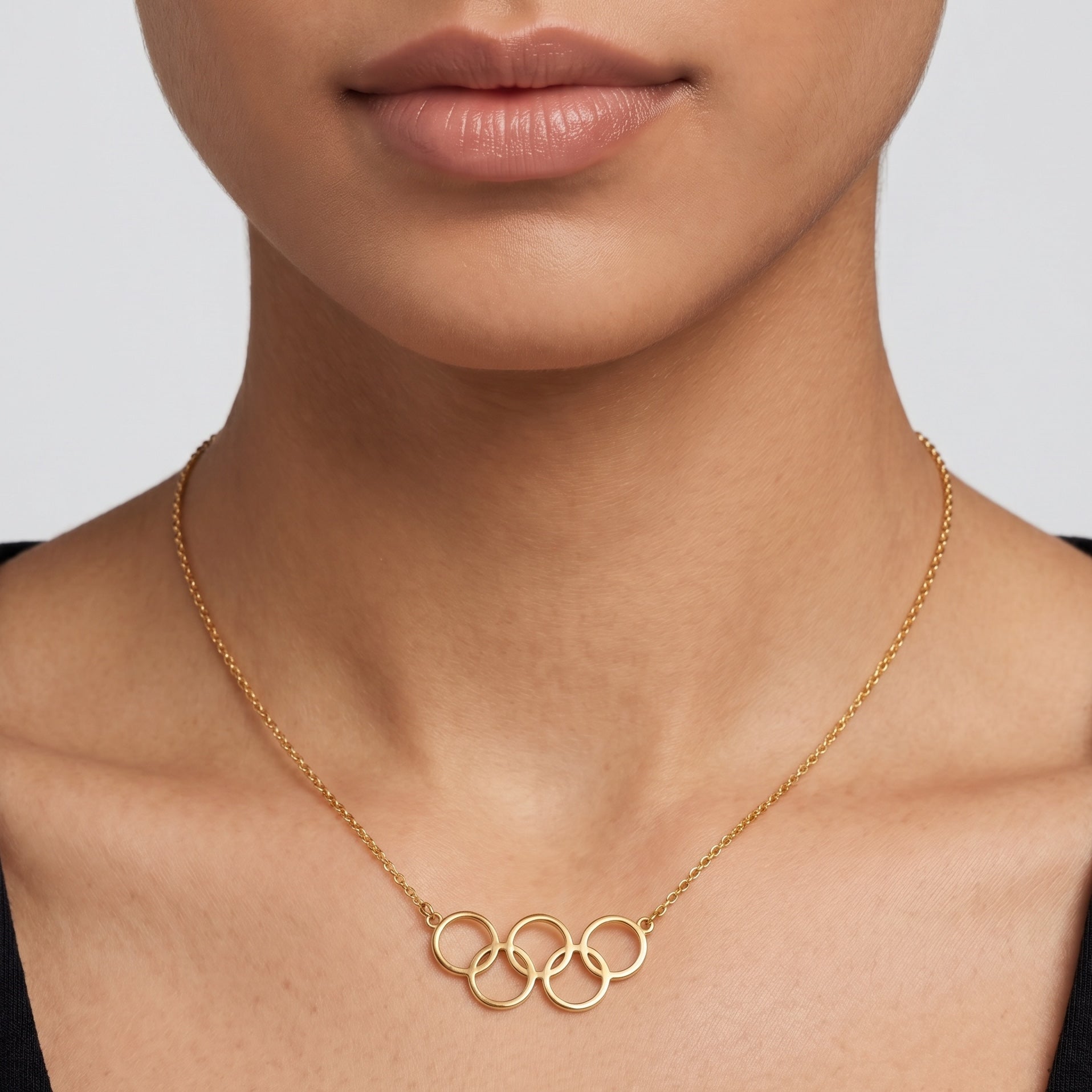 Gold necklace with interlocking rings worn by a person against a neutral background