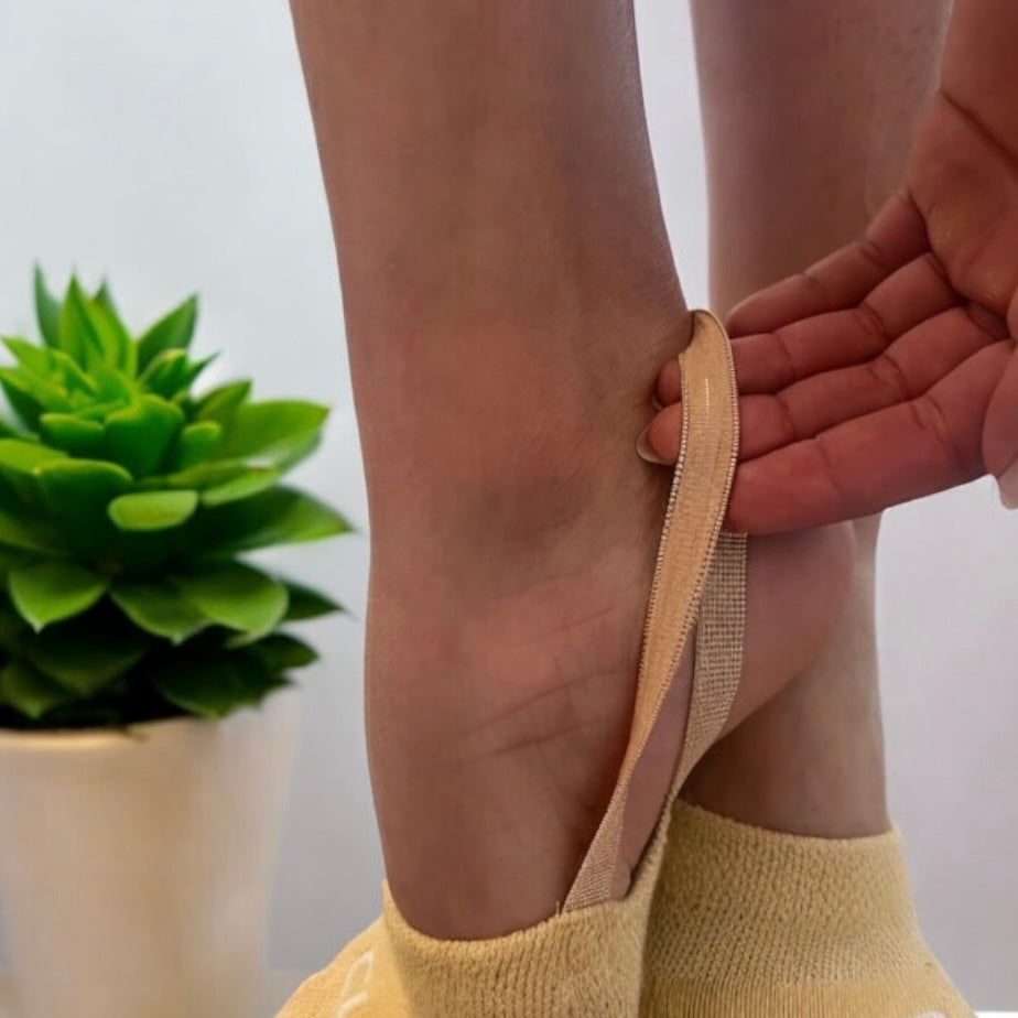 Person applying a beige bandage to their ankle with a plant in the background