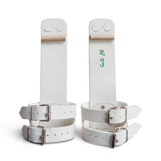 A pair of white leather wrist restraints with silver metal buckles and straps, displayed on a clean white background. One restraint features a green 'R3' monogram on the inner strap, and both have circular cutouts near the top.