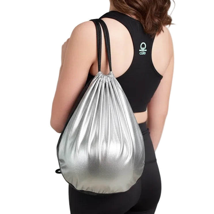 Woman wearing a black sports bra and leggings with a silver drawstring bag on a plain background