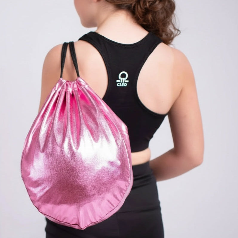 Person wearing a black sports bra with a logo and black leggings, carrying a pink drawstring bag on a light gray background.