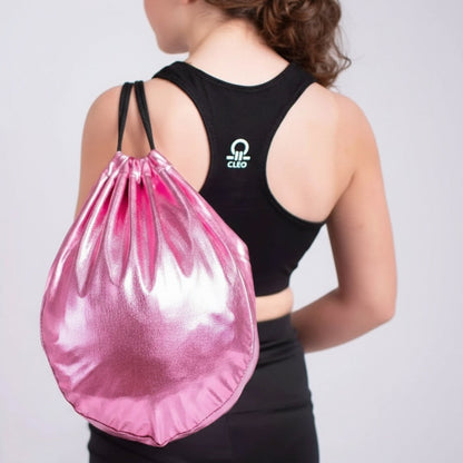 Person wearing a black sports bra with a logo and black leggings, carrying a pink drawstring bag on a light gray background.